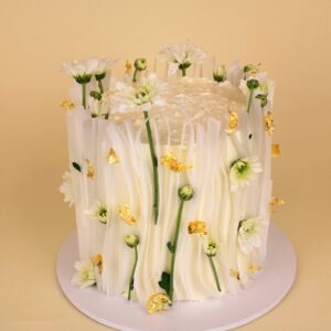 A white cake decorated with edible gold accents and small white flowers on a round base. waffle cake, engagement cake, wedding cake, floral cake