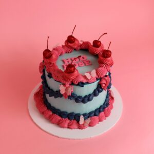 A two-tiered cake decorated with pink and blue frosting, topped with cherries and butterflies. vintage cake, retro cake, birthday cake