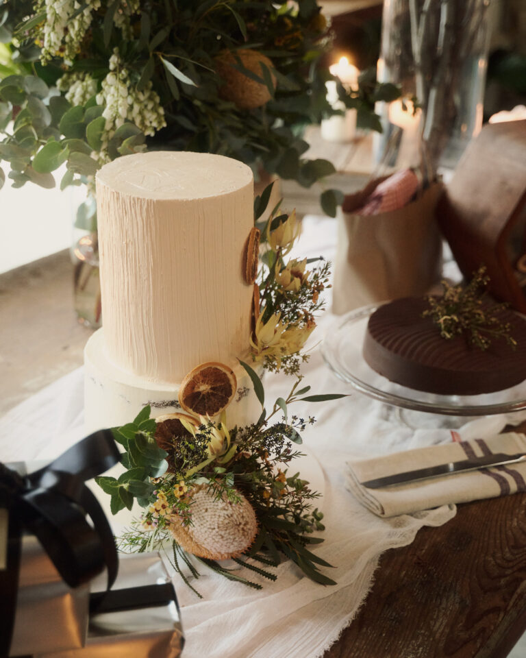 Cream textured wedding-style cake adorned with dried orange slices, eucalyptus leaves and botanical florals on a rustic table setting